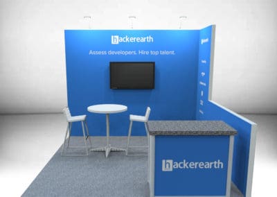 10 foot by 10 foot exhibit rental structure. 1-meter storage counter in the front, with tall table and 2 chairs. Space for monitor displays on backwall. Half-wall on the right side of the booth.