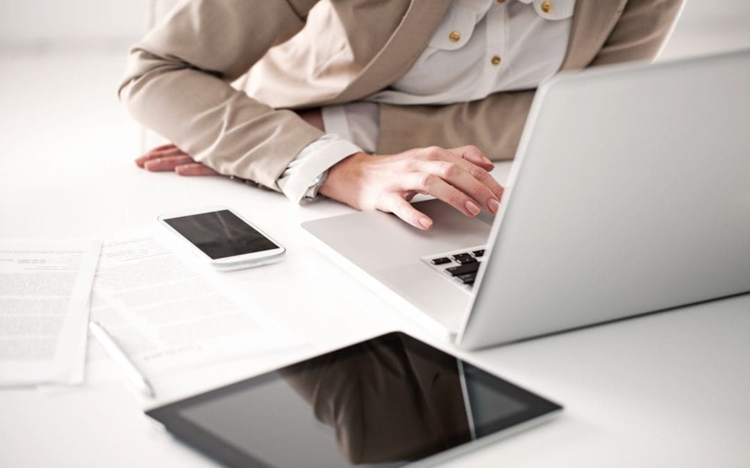 A professionally dressed person sits at their desk, leaning into their laptop