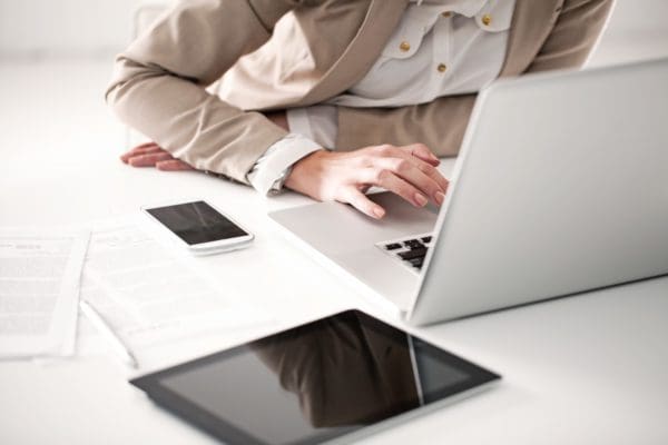 A professionally dressed person sits at their desk, leaning into their laptop