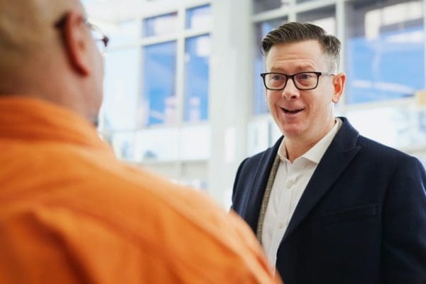 A man smiles and makes conversation with another man at a trade show