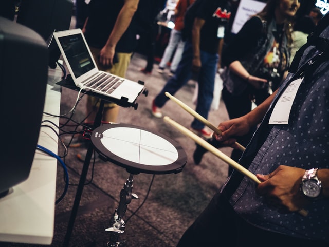 A person is playing digital drums that are connected to a laptop as trade show booth entertainment.