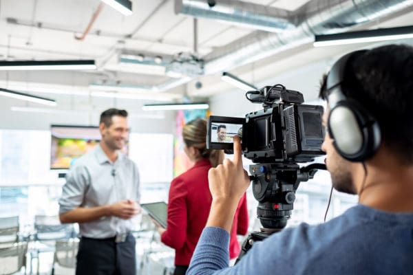 A cameraman filming two professionals. Use trade show video best practices like avoiding unnecessary sounds to make the most of your video content.