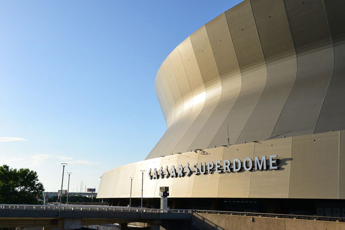 The curve of Caesars Superdome sweeps across a blue sky.