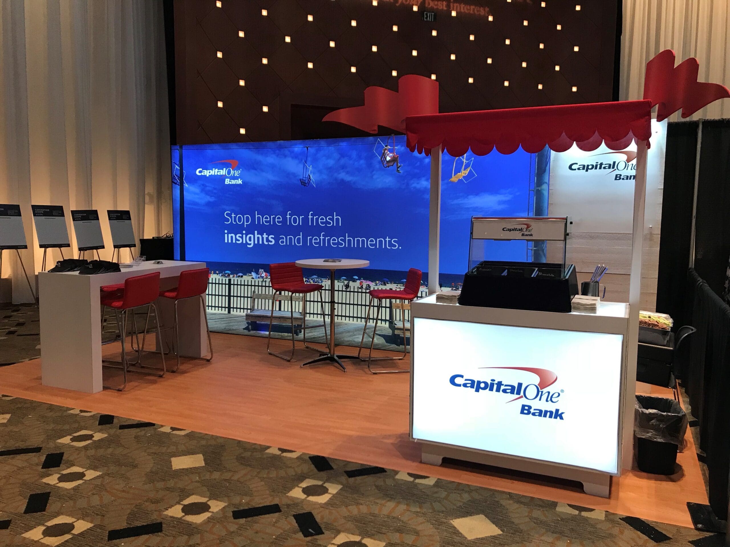 A beach themed trade show booth created by Cardinal Expo for Capital One Bank. It features an LED wall with a boardwalk scene and a kiosk for serving ice cream.