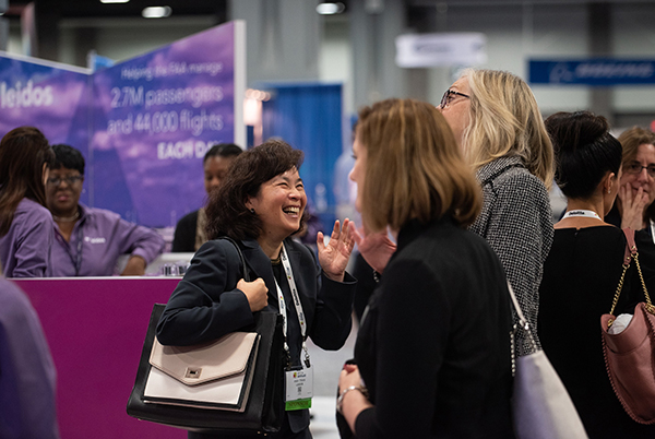 ATCA conference attendees laugh and chat in front of display booths on the exhibit floor.