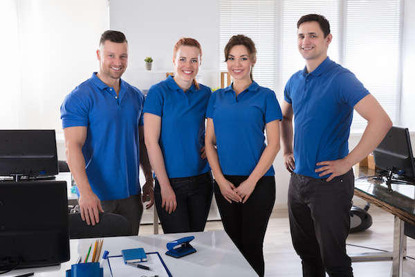 A group of four employees wearing matching blue polo shirts so they're easily identified at their booth. Find more trade show attire ideas like this in our blog post.
