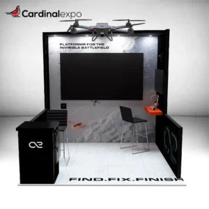 Straight-on view of a 10x10 display showcasing a large TV, hanging drone prop, reception desk, and workstation.