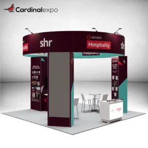 Front-left view of a 20x20 island exhibit highlighting a round header beam, graphic pillars, backlit desk, and meeting area.