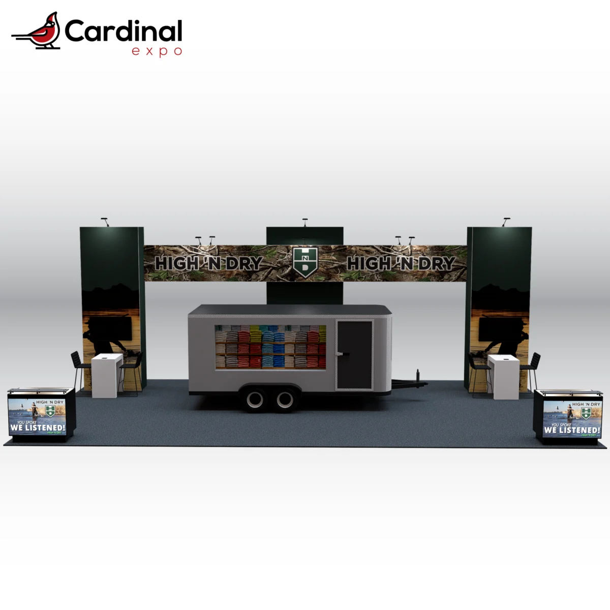 Front view of a large custom trade show booth rental featuring a central utility trailer display,overhead header beam, high-top workstation desks, and front branding counters.